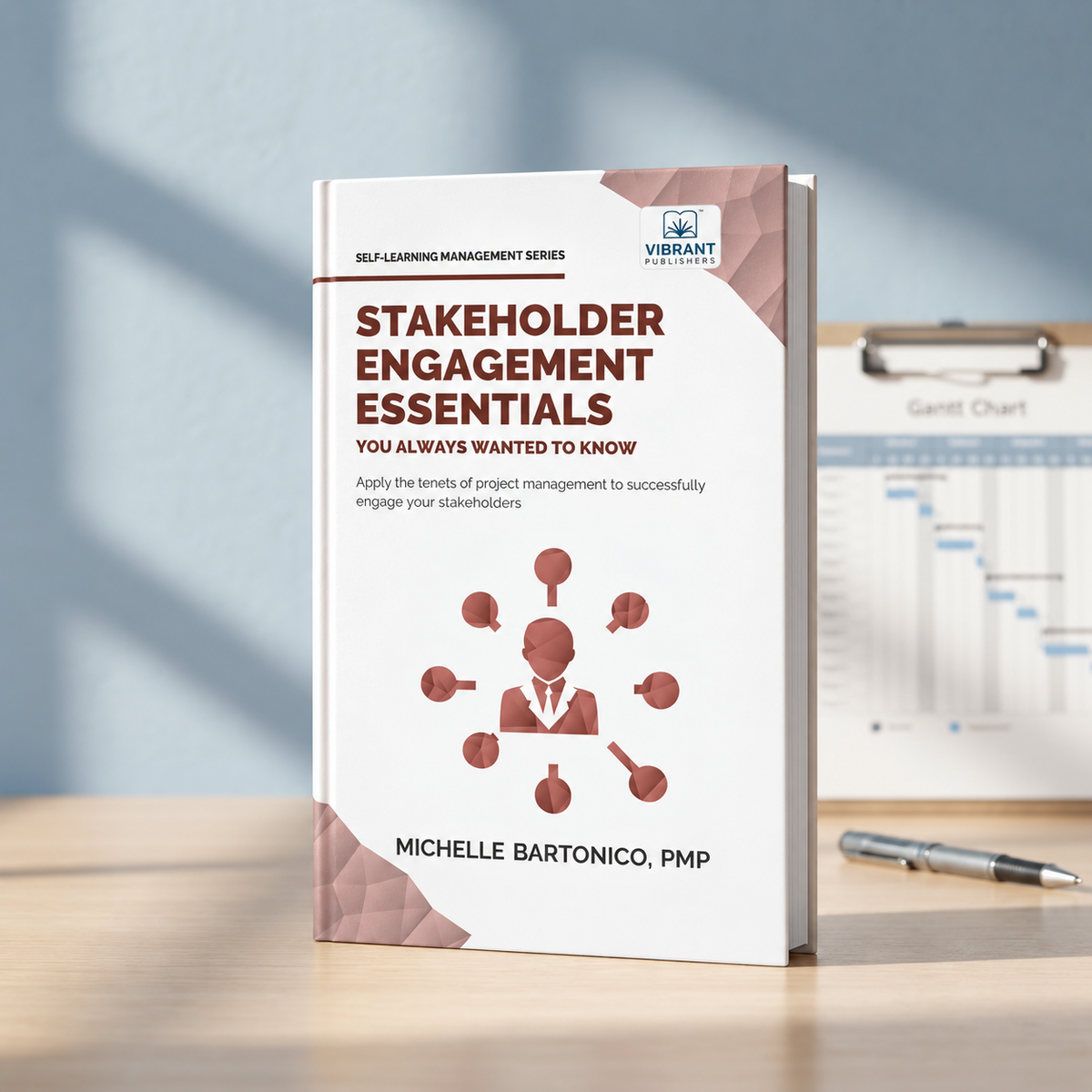 A paperback book titled 'Stakeholder Engagement Essentials' by Michelle Bartonico, PMP, standing upright on a light wood desk. 