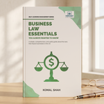 A paperback book titled "Business Law Essentials" by Komal Shah stands upright on a wooden surface. The cover is off-white with green text and geometric accents, featuring a green scale-and-dollar symbol.