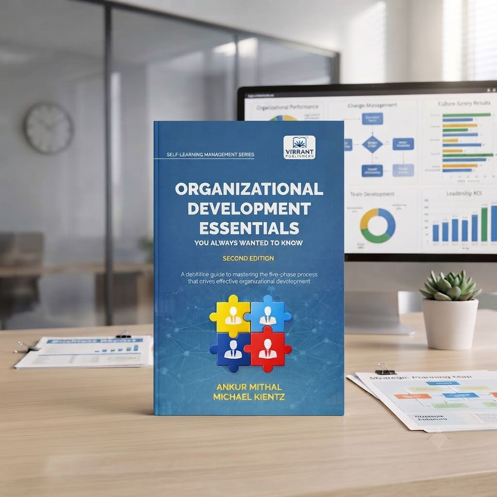 A book titled "Organizational Development Essentials" stands upright on a desk in front of a computer monitor showing charts and graphs. 