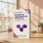 A book titled 'Diversity in the Workplace Essentials' by Jaquina Gilbert stands open on a wooden desk in a warm, softly lit room. 